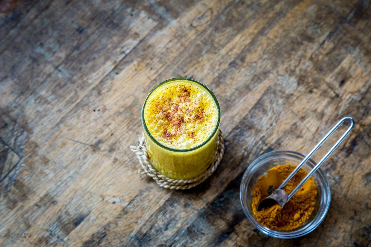Glas Goldene Milch, daneben gemahlene Kurkuma
