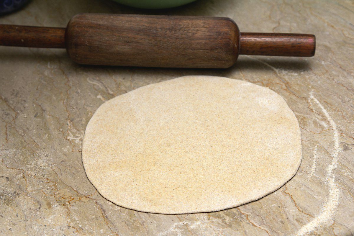 Ausgerollter Teigfladen mit einem Nudelholz auf Holz