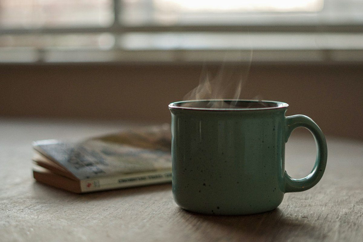 Dampfender grüner Becher neben einem Buch auf einem Fensterbrett