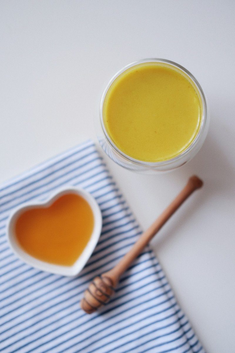 Glas Goldene Milch, daneben ein herzförmiges Schälchen Honig und ein Honiglöffel