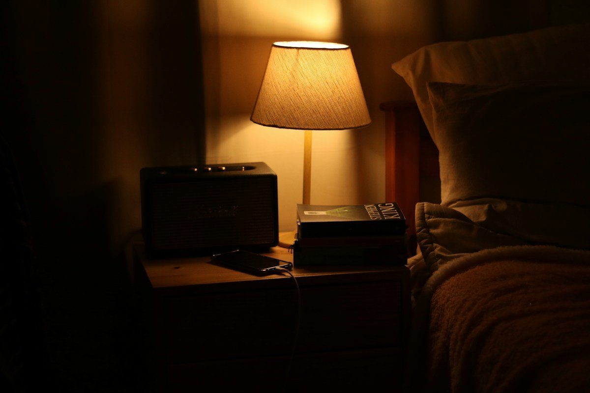 Nachttischlampe mit Stoffschirm neben einem Bett in einem dunklen Zimmer
