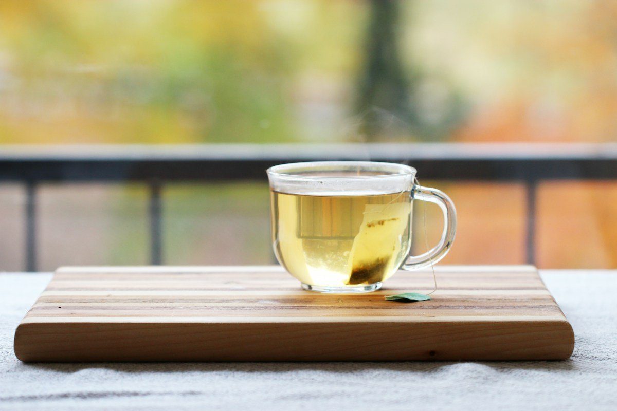 Teeglas mit hellem Tee auf einem Holzbrett im Freien